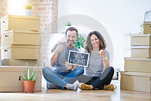 Middle age senior couple sitting on the floor holding blackboard moving to a new home happy with big smile doing ok sign, thumb up