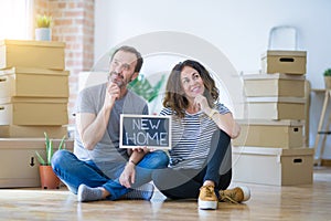 Middle age senior couple sitting on the floor holding blackboard moving to a new home serious face thinking about question, very
