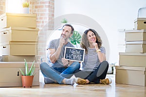 Middle age senior couple sitting on the floor holding blackboard moving to a new home serious face thinking about question, very