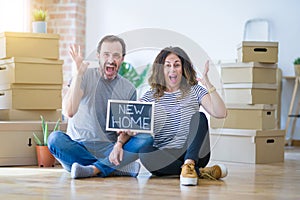 Middle age senior couple sitting on the floor holding blackboard moving to a new home very happy and excited, winner expression