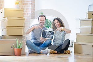 Middle age senior couple sitting on the floor holding blackboard moving to a new home very happy pointing with hand and finger