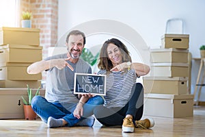 Middle age senior couple sitting on the floor holding blackboard moving to a new home very happy pointing with hand and finger