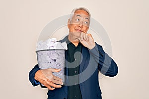 Middle age senior grey-haired business man holding paper bin full of rubbish documents serious face thinking about question, very