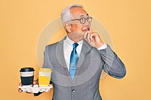 Middle age senior grey-haired business man wearing glasses holding coffee cup on tray serious face thinking about question, very