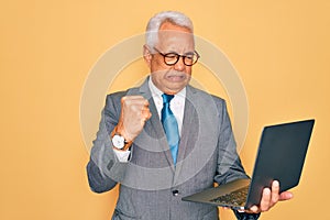 Middle age senior grey-haired business man wearing glasses working using computer laptop annoyed and frustrated shouting with