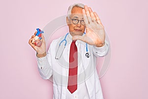 Middle age senior grey-haired cardiologist doctor man holding professional medicine heart with open hand doing stop sign with