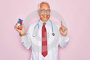 Middle age senior grey-haired cardiologist doctor man holding professional medicine heart surprised with an idea or question