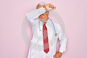 Middle age senior grey-haired doctor man wearing stethoscope and professional medical coat covering eyes with arm, looking serious