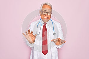 Middle age senior grey-haired doctor man wearing stethoscope and professional medical coat disgusted expression, displeased and