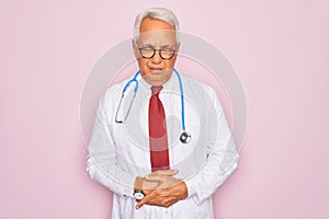 Middle age senior grey-haired doctor man wearing stethoscope and professional medical coat with hand on stomach because
