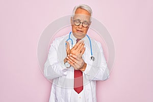 Middle age senior grey-haired doctor man wearing stethoscope and professional medical coat Suffering pain on hands and fingers,