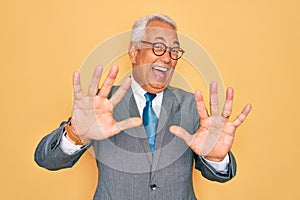 Middle age senior grey-haired handsome business man wearing glasses over yellow background afraid and terrified with fear