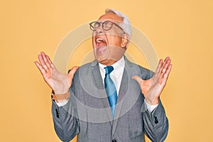 Middle age senior grey-haired handsome business man wearing glasses over yellow background celebrating mad and crazy for success