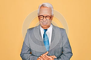 Middle age senior grey-haired handsome business man wearing glasses over yellow background with hand on stomach because