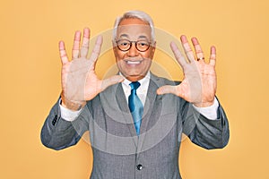 Middle age senior grey-haired handsome business man wearing glasses over yellow background showing and pointing up with fingers