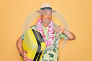 Middle age senior grey-haired man on holiday holding vacation suitcase over yellow background with angry face, negative sign