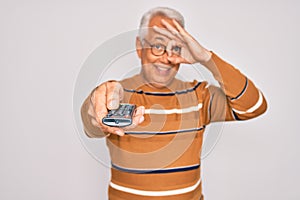 Middle age senior grey-haired man using tv remote control watching television with happy face smiling doing ok sign with hand on