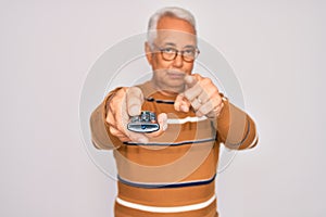 Middle age senior grey-haired man using tv remote control watching television pointing with finger to the camera and to you, hand