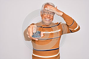 Middle age senior grey-haired man using tv remote control watching television stressed with hand on head, shocked with shame and