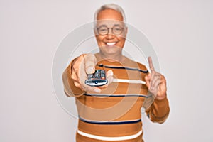 Middle age senior grey-haired man using tv remote control watching television surprised with an idea or question pointing finger