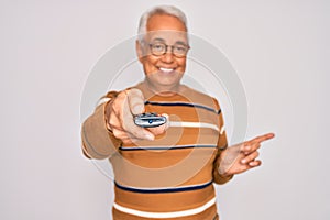 Middle age senior grey-haired man using tv remote control watching television very happy pointing with hand and finger to the side