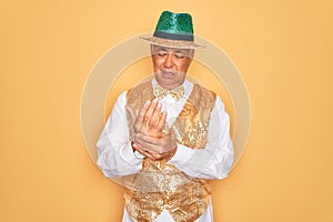 Middle age senior grey-haired man wearing Brazilian carnival custome over yellow background Suffering pain on hands and fingers,