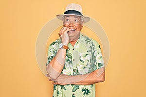 Middle age senior grey-haired man wearing summer hat and floral shirt on beach vacation looking stressed and nervous with hands on
