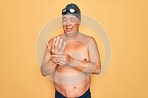 Middle age senior grey-haired swimmer man wearing swimsuit, cap and goggles Suffering pain on hands and fingers, arthritis