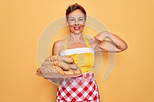 Middle age senior housewife pin up woman wearing 50s style retro dress cooking wholemeal bread with surprise face pointing finger