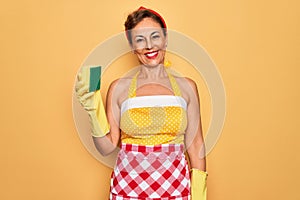 Middle age senior housewife pin up woman wearing 50s style retro dress using cleaner scrub with a happy face standing and smiling