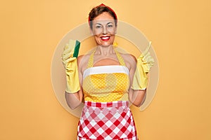 Middle age senior housewife pin up woman wearing 50s style retro dress using cleaner scrub very happy pointing with hand and