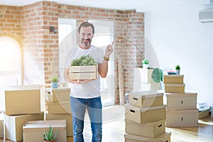 Middle age senior man moving to a new house packing cardboard boxes very happy pointing with hand and finger to the side