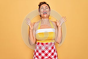 Middle age senior pin up housewife woman wearing 50s style retro dress and apron celebrating mad and crazy for success with arms