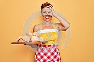 Middle age senior pin up housewife woman wearing 50s style retro dress and apron cooking bread with happy face smiling doing ok