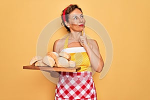Middle age senior pin up housewife woman wearing 50s style retro dress and apron cooking bread serious face thinking about