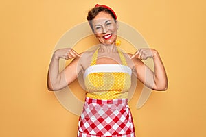 Middle age senior pin up housewife woman wearing 50s style retro dress and apron looking confident with smile on face, pointing