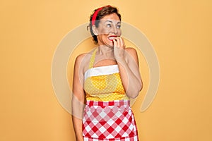 Middle age senior pin up housewife woman wearing 50s style retro dress and apron looking stressed and nervous with hands on mouth