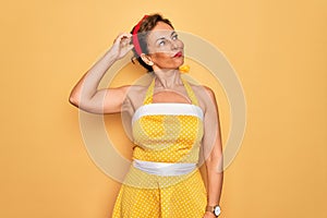Middle age senior pin up woman wearing 50s style retro dress over yellow background confuse and wondering about question