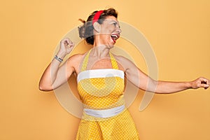 Middle age senior pin up woman wearing 50s style retro dress over yellow background Dancing happy and cheerful, smiling moving