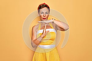 Middle age senior pin up woman wearing 50s style retro dress over yellow background Doing time out gesture with hands, frustrated