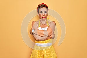 Middle age senior pin up woman wearing 50s style retro dress over yellow background shaking and freezing for winter cold with sad