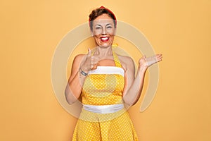 Middle age senior pin up woman wearing 50s style retro dress over yellow background Showing palm hand and doing ok gesture with