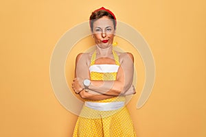 Middle age senior pin up woman wearing 50s style retro dress over yellow background skeptic and nervous, disapproving expression