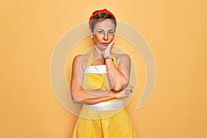 Middle age senior pin up woman wearing 50s style retro dress over yellow background thinking looking tired and bored with