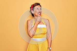 Middle age senior pin up woman wearing 50s style retro dress over yellow background Thinking worried about a question, concerned