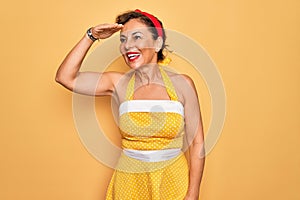 Middle age senior pin up woman wearing 50s style retro dress over yellow background very happy and smiling looking far away with