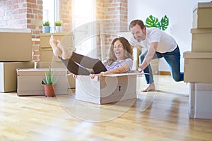 Middle age senior romantic couple having fun riding inside of cardboard, excited and smiling happy for moving to a new home