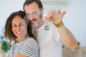 Middle age senior romantic couple holding and showing house keys, hugging and smiling happy for moving to a new home