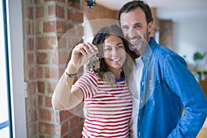 Middle age senior romantic couple holding and showing house keys smiling happy for moving to a new home