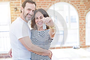 Middle age senior romantic couple holding and showing house keys smiling happy for moving to a new home